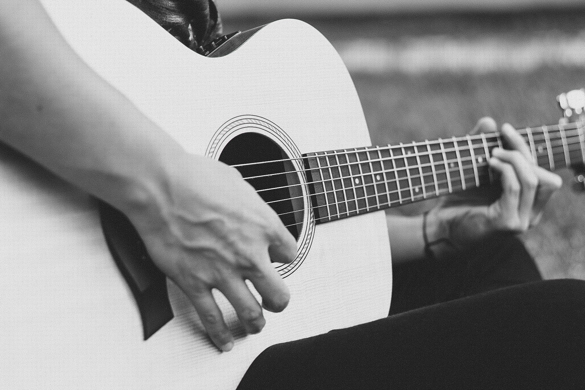 Detalhe de um violão acústico sendo tocado, em preto e branco